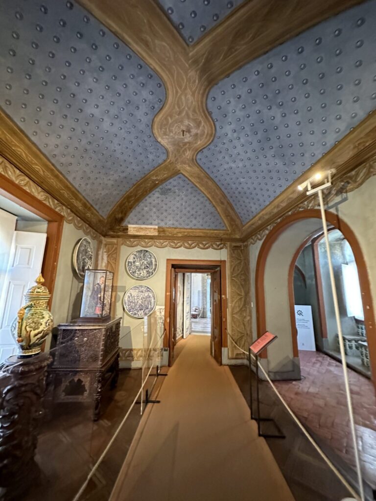 Interior museum gallery with ornate wooden architectural details, perforated ceiling panels, and decorative Asian plates displayed on cream-colored walls