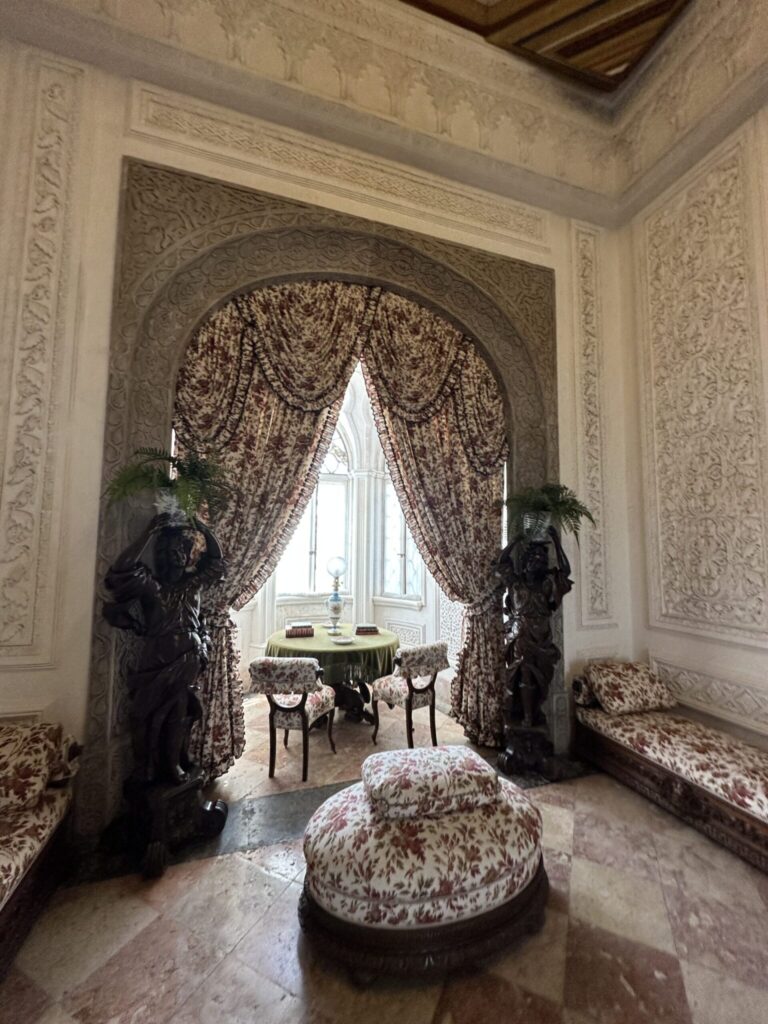 An ornate neoclassical room with decorative plaster walls, dark bronze statues flanking a draped archway, and patterned furnishings