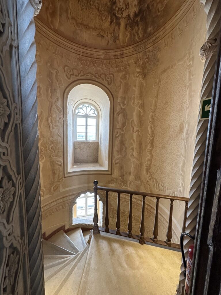 Elegant spiral staircase with ornate damask wallpaper and arched window in classical architectural interior