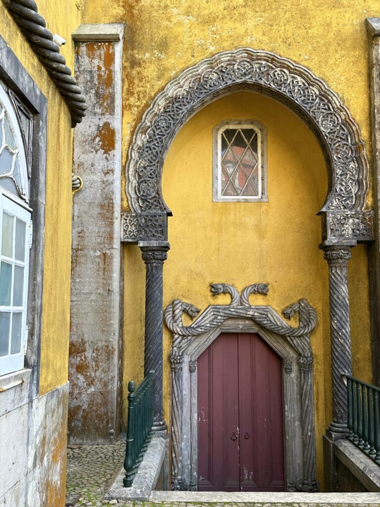 Ornate arched doorway with burgundy door set into vibrant yellow building facade with decorative stone carvings