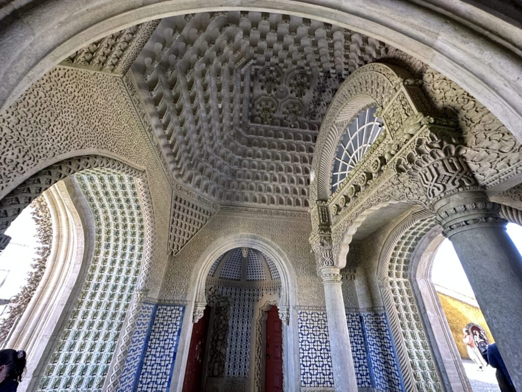Ornate Islamic architecture featuring intricate geometric patterns, carved ceilings, blue tile work, and arched doorways in a palace or mosque interior