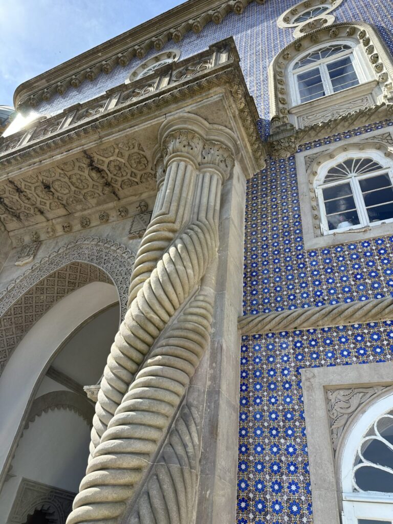 Ornate stone column with fluted detailing beside a blue and white tiled facade with decorative windows