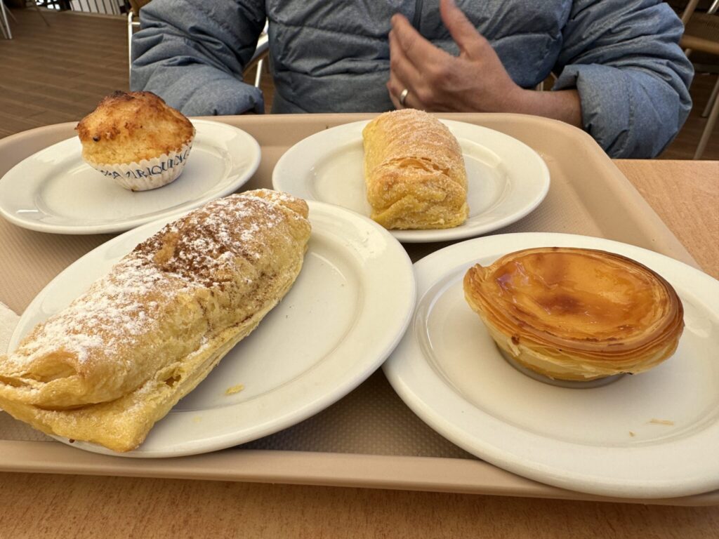 Four pastries on white plates arranged on a tray with a person in a blue jacket seated behind them