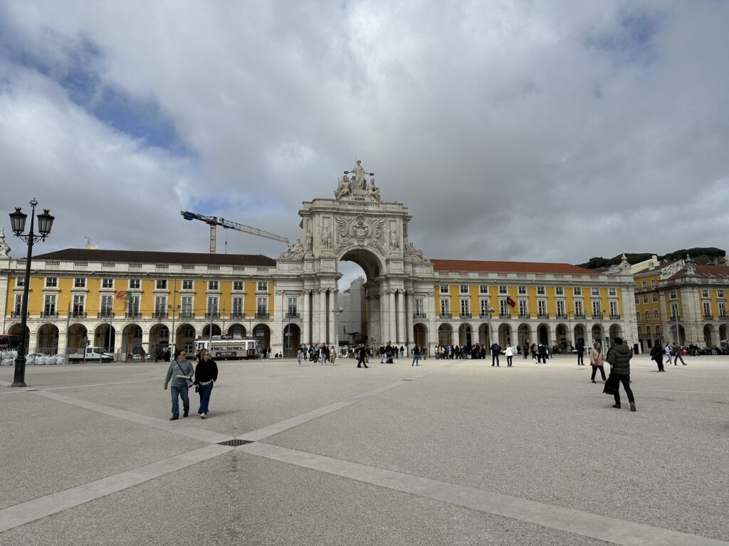 Praça do Comércio square in Lisbon with yellow arcaded buildings and white triumphal arch under cloudy sky