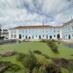 Light blue colonial buildings with green shutters overlook a waterway filled with algae and aquatic vegetation