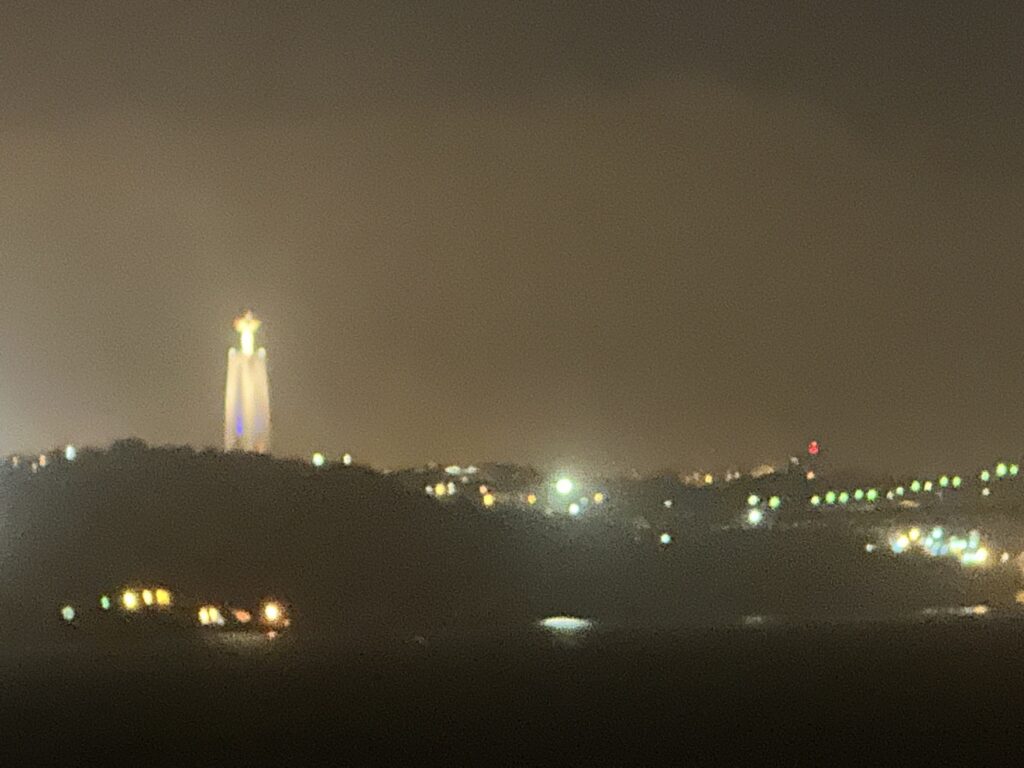 Illuminated monument tower on hilltop at night with city lights scattered across the landscape below