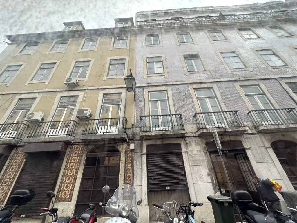 Historic European building facade with multiple windows, wrought-iron balconies, and shuttered storefronts on ground level