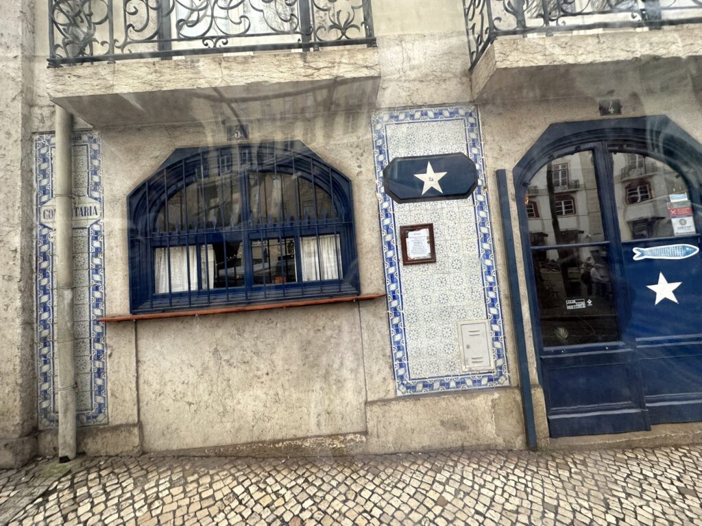 Weathered Portuguese storefront with blue-framed window and door decorated with white stars and traditional azulejo tiles