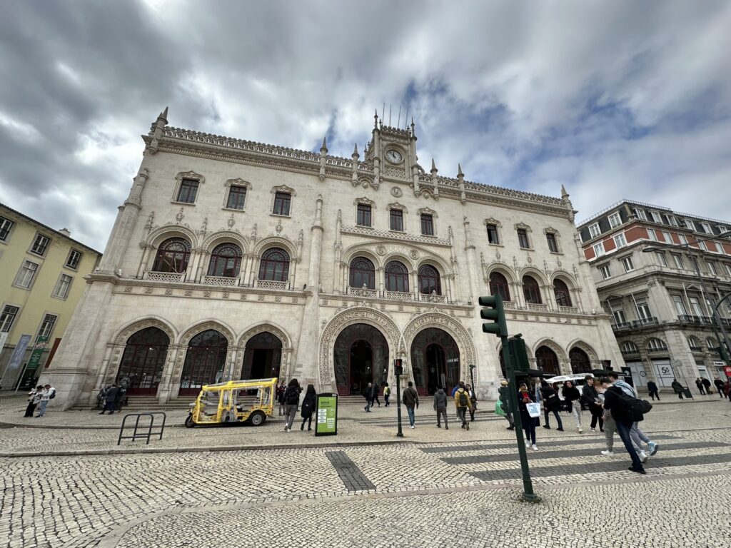 Historic white stone building with ornate architecture and multiple arches in a European city square with pedestrians