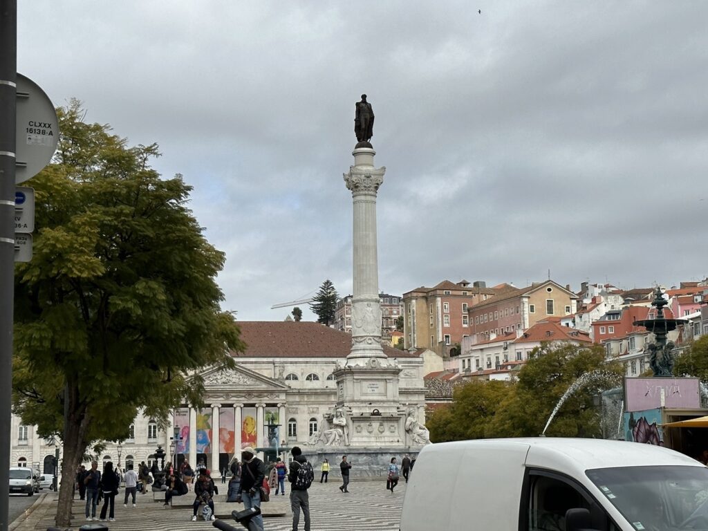 Monument column with statue on top in European city square surrounded by historic buildings and tourists
