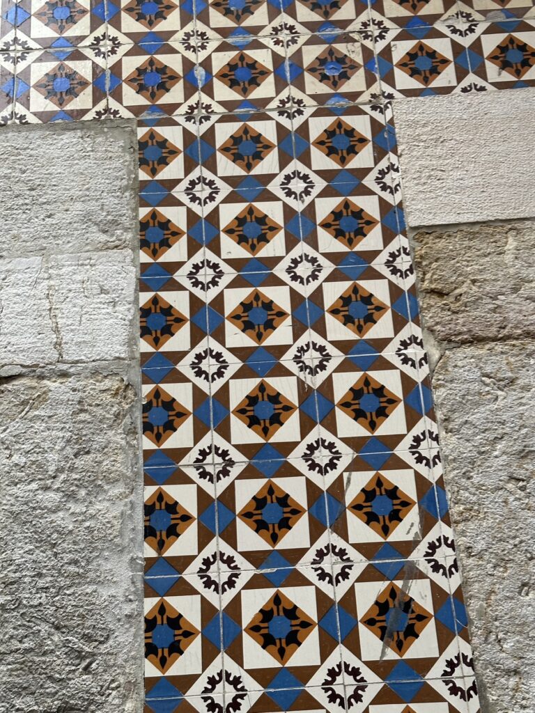 Ornate ceramic tiles with blue, brown, and black geometric patterns mounted on weathered stone wall