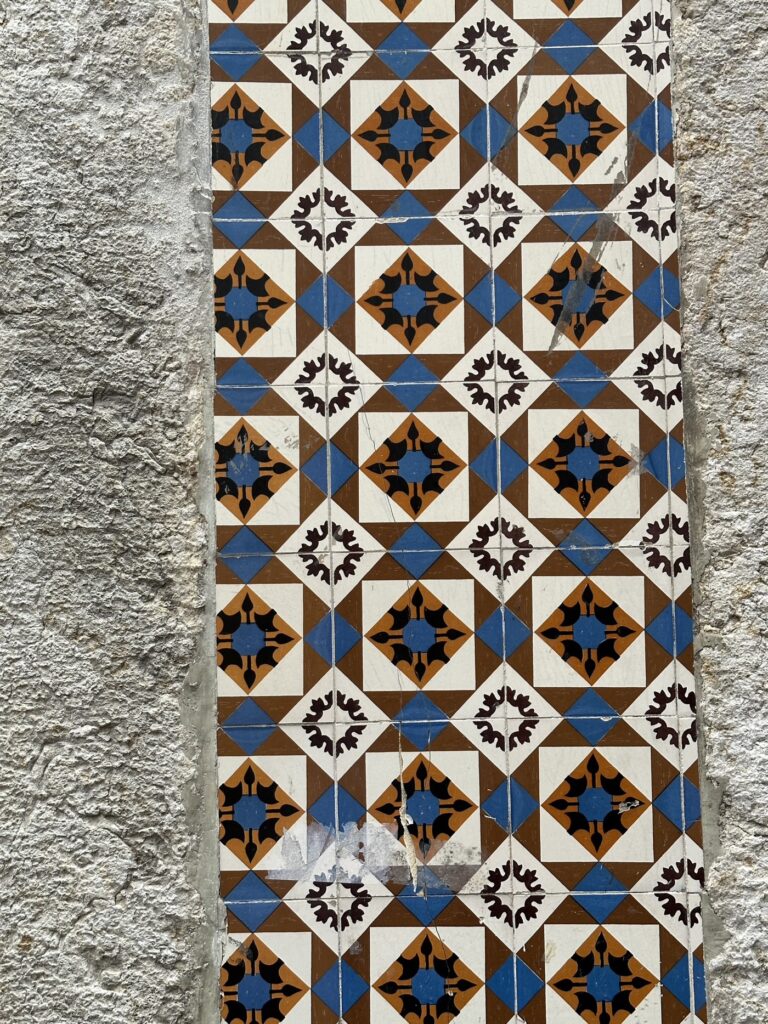 Ornate ceramic tiles with geometric patterns in blue, brown, and cream arranged vertically on a weathered stone wall