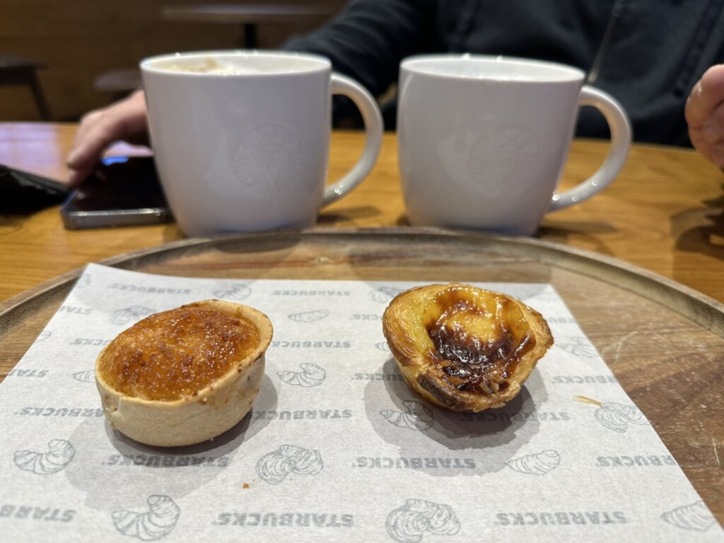Two pastries on parchment paper sit before white mugs on a wooden table during a beverage service
