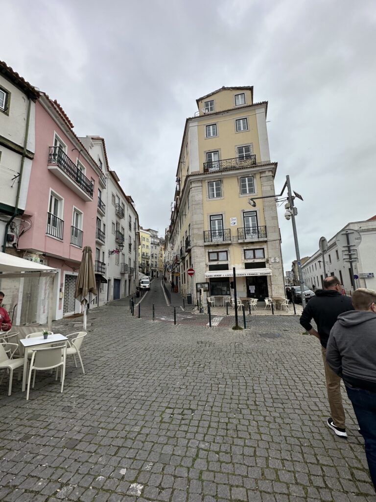 A historic European street scene with colorful pastel buildings, cobblestone plaza, and overcast sky