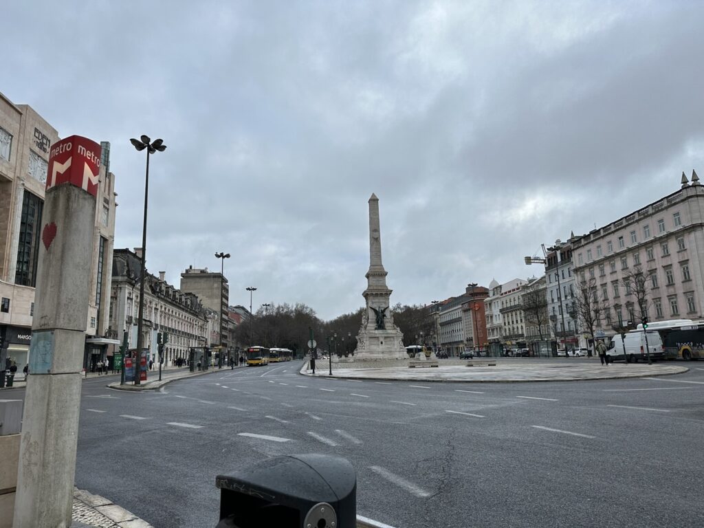 A monumental obelisk stands centered in a large European city square surrounded by classical buildings and bare winter trees